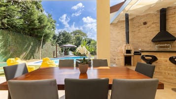 An outdoor dining area with a brick wall, a brick oven, and a view of a swimming pool.