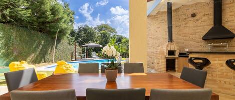 An outdoor dining area with a brick wall, a brick oven, and a view of a swimming pool.