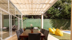 A covered patio with a dining table, chairs, and yellow bean bags.
