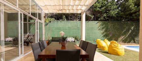 A covered patio with a dining table, chairs, and yellow bean bags.