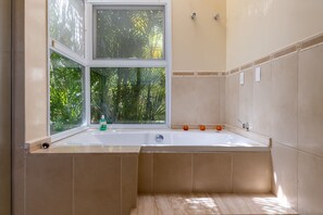 A bathroom with a bathtub, a window, and a view of greenery outside. - Casa com 4 Quartos - Alto Padrão (Carapicuíba)