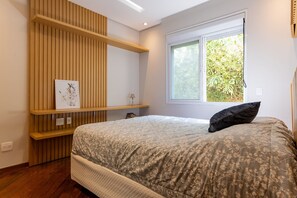 Ein Schlafzimmer mit einem Bett, einem Fenster mit Blick auf Grünflächen, einer Holzablage mit einem Bild und einem Nachttisch.