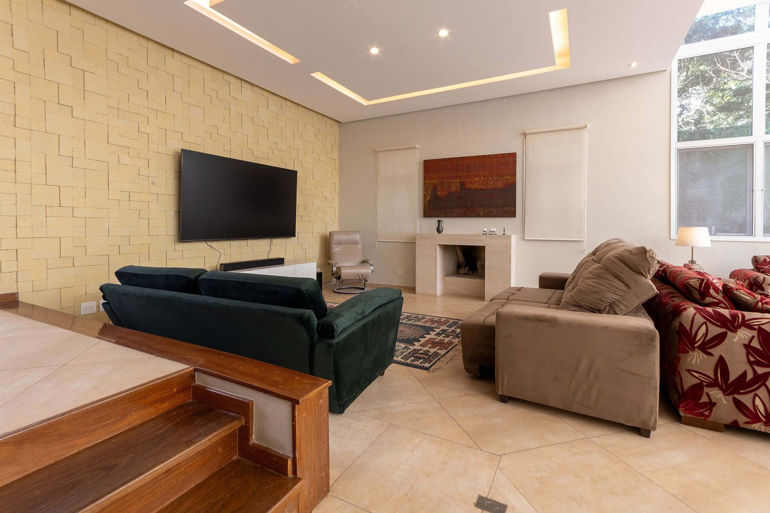 A modern living room with a flat-screen TV, two sofas, a fireplace, and a large window.