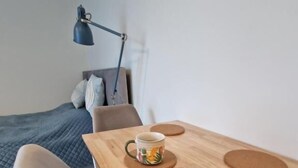 Una habitación pequeña y acogedora con una mesa de madera, dos sillas, una cama con manta azul y una lámpara de escritorio.