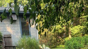 Eine Terrasse mit Adirondack-Stühlen, einer Steinkaminfeuerstelle und einem Haus im Hintergrund.