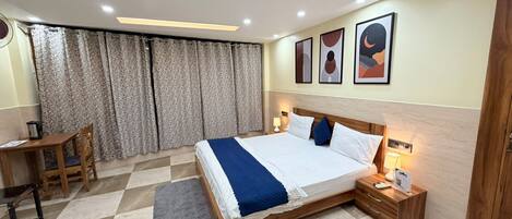 A hotel room with a large bed, a desk, a chair, and a window with curtains.
