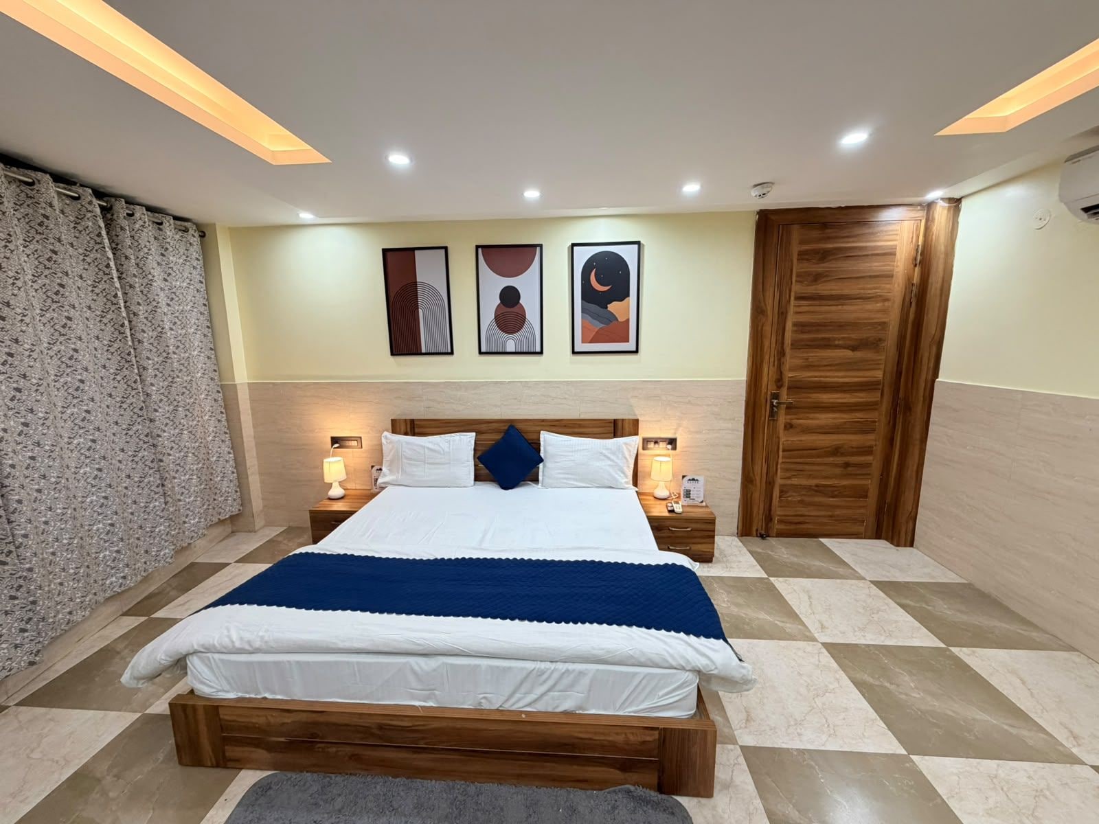 Une chambre d’hôtel avec un lit, des tables de chevet, une armoire en bois et des œuvres d’art accrochées au mur.