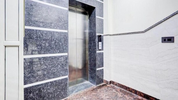 A modern elevator with a metallic interior, adjacent to a wall with a marble pattern and a white panel. - Hotel Elite INN (Dehradun)