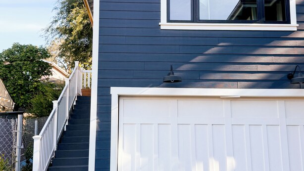 Une maison à deux étages avec une porte de garage blanche, un escalier extérieur et un jardinier en métal orné de fleurs.