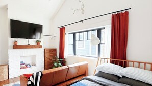 Une chambre à coucher avec un lit, un ventilateur de plafond, une cheminée, une télévision et une fenêtre avec des rideaux.