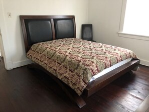 Ein Schlafzimmer mit einem Holzbettgestell, einer gestreiften Bettdecke, einem Nachttisch und einem Fenster.