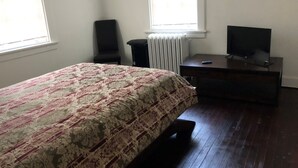 A bedroom with a bed, a chair, a desk with a TV, and a radiator. - 2-bedroom building in cool Richmond with refreshing AC (Richmond)