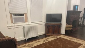 A living room with a radiator, a television on a wooden cabinet, a patterned rug, and a fireplace. - 2-bedroom building in cool Richmond with refreshing AC (Richmond)