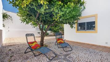 Un patio con dos sillones, un árbol y una pared blanca con una ventana.