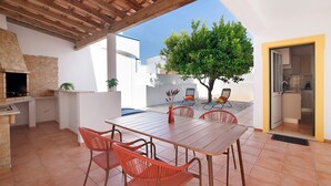 An outdoor patio with a wooden table and chairs, a stone fireplace, and a view of a tree and buildings in the background. - Villa 'Modern  in Olhao' with Mountain View, Wi-Fi and Air Conditioning (Quelfes)