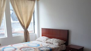 Un dormitorio con cama, mesita de noche, ventana con cortinas y vista al exterior.