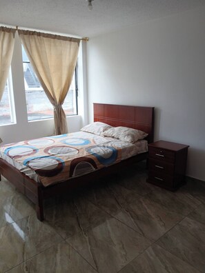 Un dormitorio con cama, mesita de noche, ventana con cortinas y vista al exterior.