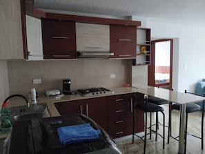 Una cocina con estufa, lavaplatos y taburetes de bar.