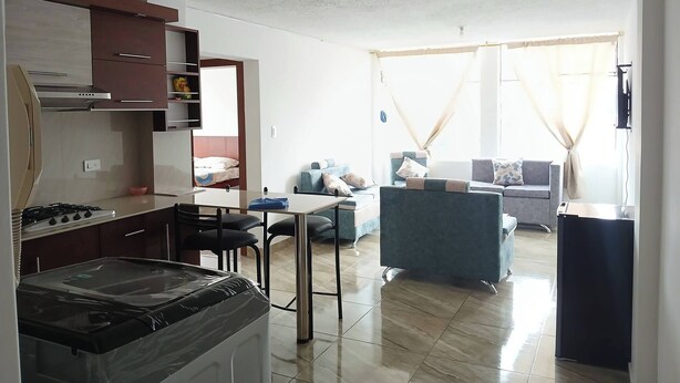 Un espacio habitable compacto con kitchenette, zona de comedor y sala de estar con sofá y sillones.