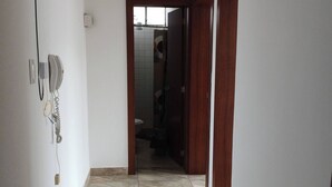 Un pasillo con suelo de baldosas, una puerta que da al baño y un teléfono instalado en la pared.