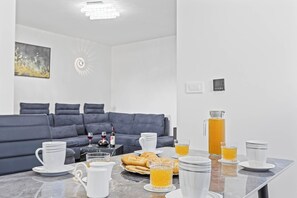 Ein modernes Wohnzimmer mit einem grauen Sofa, einem Couchtisch mit Frühstücksgebäck und minimalistischer Einrichtung.