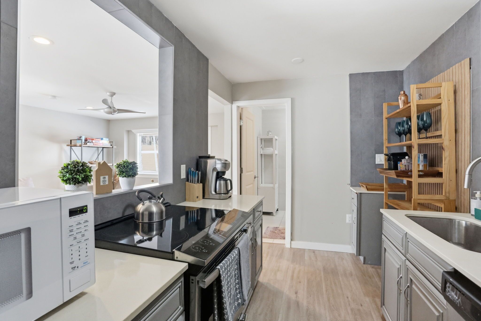 A modern kitchen with a microwave, stove, and sink, wooden shelves, and a ceiling fan.