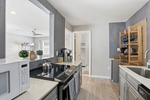 A modern kitchen with a microwave, stove, and sink, wooden shelves, and a ceiling fan. - Tropical Pool Oasis Near Atlantic Ave & Beach (Delray Beach)