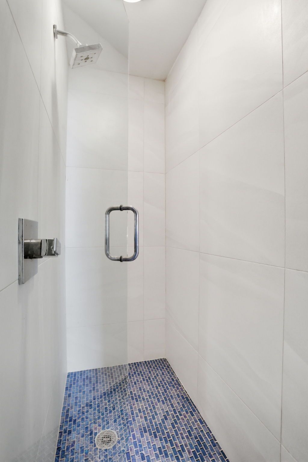 A shower with a chrome showerhead, a grab bar, and a blue-tiled floor.