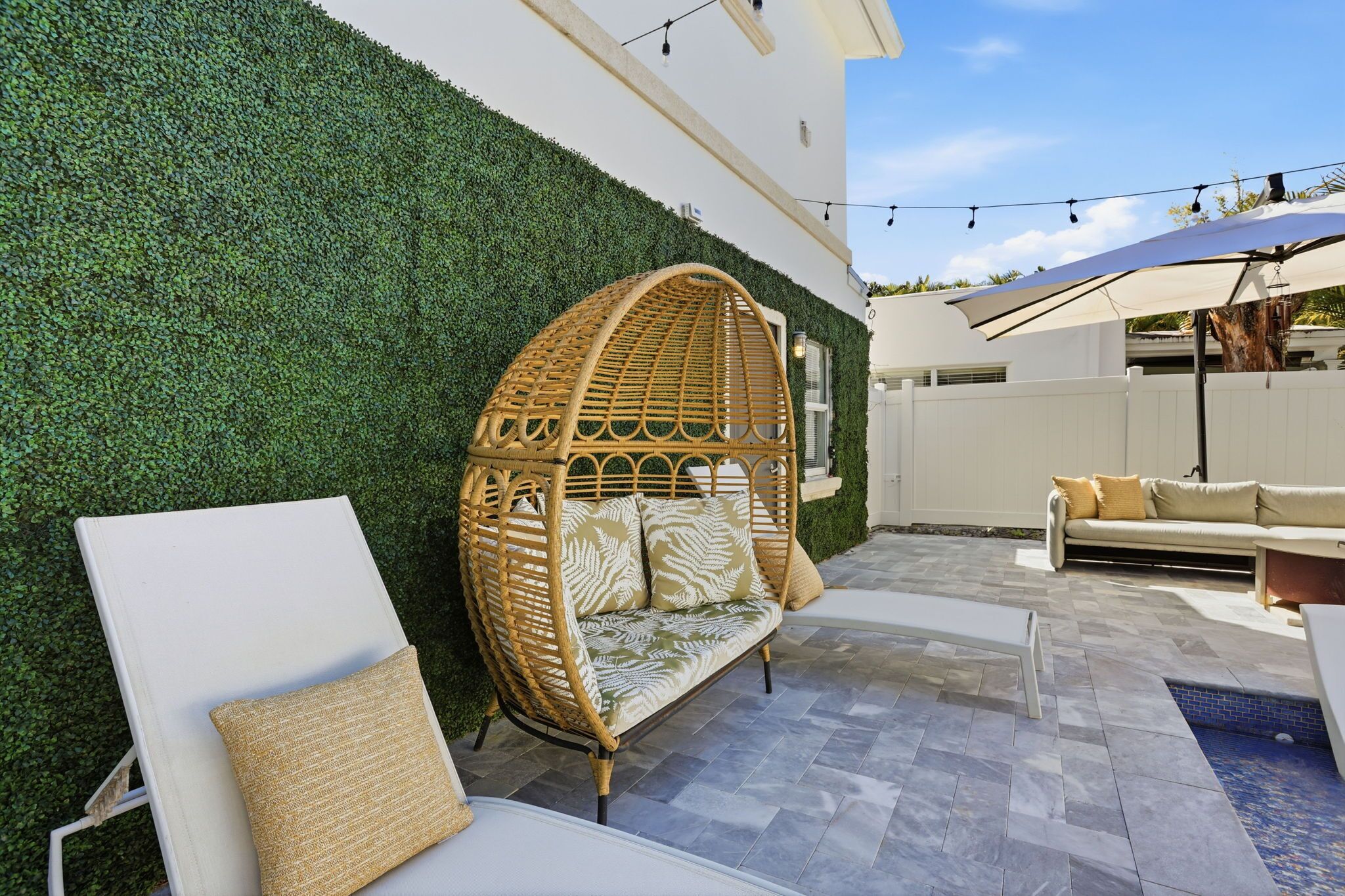 A patio with a white lounge chair, a wicker sofa, and a white couch.