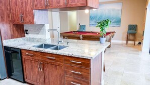 Una cocina con armarios de madera, encimera de mármol, lavavajillas empotrado y una mesa de billar.