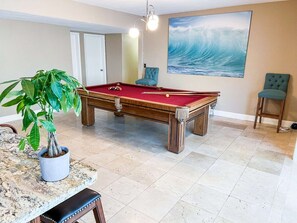 A pool table in a room with a large wave painting, a potted plant, and two chairs. - Luxurious Oasis - Heated Salt Pool - Pool Table - 4BR Near Miami (Cutler Bay)