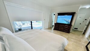 Un dormitorio con una cama grande, televisión y vista al océano a través de una puerta corrediza.