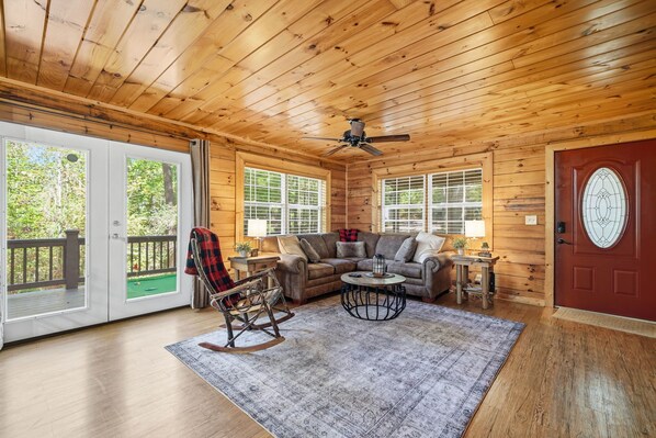L’intérieur d’un chalet en bois, avec un fauteuil à bascule, un canapé et un ventilateur de plafond.