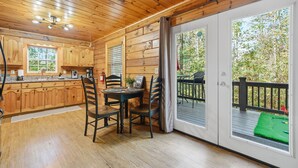 Una baita di legno con angolo cottura, zona pranzo e terrazza con un tappetino verde.