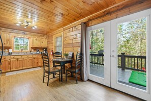 L’intérieur d’un chalet en bois comprend un coin repas, une cuisine et une terrasse dotée d’un tapis vert.