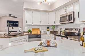 A modern kitchen with white cabinets, a microwave, stove, and a large island with a cutting board and glasses. - Scottsdale 4 Bdrm Retreat, Pool, Spa, Prime Location! (Scottsdale)