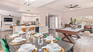 Ampla sala de estar com mesa de bilhar, mesa de jantar para seis pessoas e cozinha ao fundo.