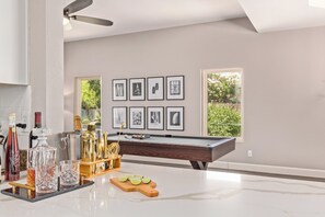 A modern living room with a pool table, framed artwork on the wall, and a view of greenery outside. - Scottsdale 4 Bdrm Retreat, Pool, Spa, Prime Location! (Scottsdale)