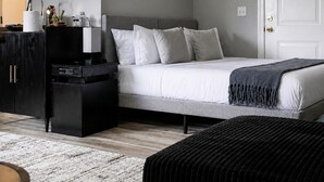 Een slaapkamer met een bed, nachtkastjes, een dressoir, een neonbord en een deur.