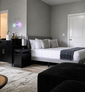 Ein Schlafzimmer mit Bett, Nachttischen, einem Schminktisch und einer Tür, sowie einem Neon-Schild.