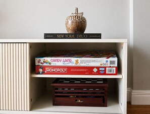 Ein Regal mit einem Monopoly-Spiel, einem Buch mit dem Titel 'New York Deco' und einer Dekorationsvase.