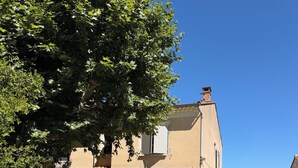 Ein zweigeschossiges Haus mit Terrasse, Gartenmöbeln und einem großen Baum, der Schatten spendet.