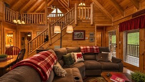 Ein Blockhaus-Interieur mit Treppe, Holzwänden, Essbereich und Wohnzimmer mit Sofa und Kissen.