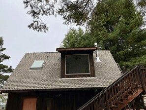A house with a sloped roof, a skylight, and a wooden staircase leading to a deck.