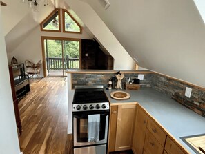 A kitchen with a stone backsplash, wooden cabinets, and a large window overlooking greenery.