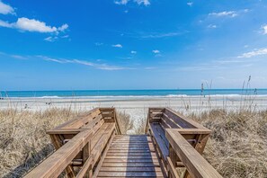 Un paseo marítimo de madera que lleva a una playa con cielos despejados y vistas al océano.