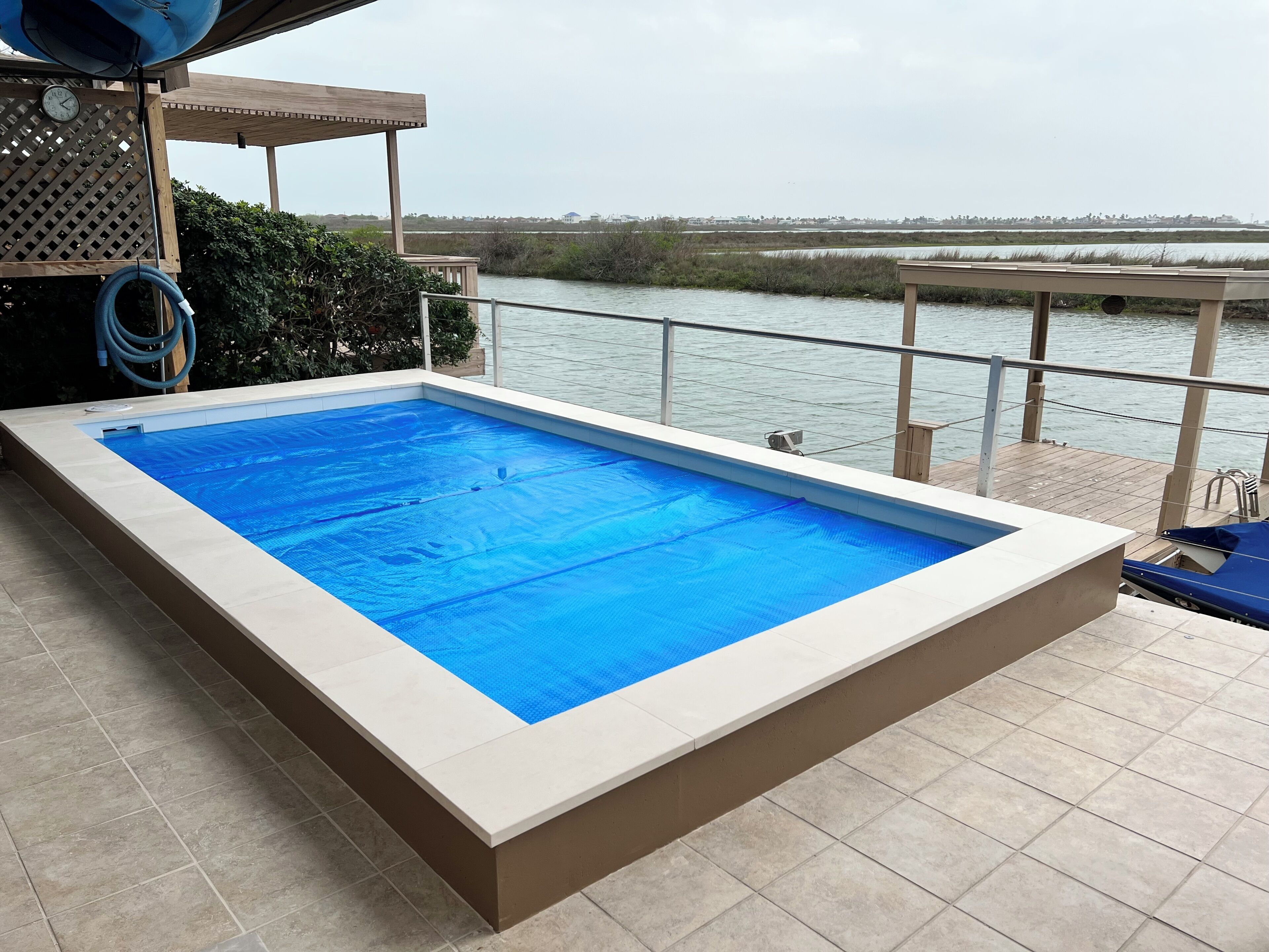 Una piscina rectangular con cubierta azul, rodeada por una solana con baldosas, con vistas a una masa de agua.