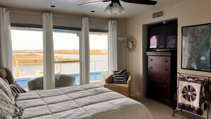 Un dormitorio con cama, una silla, cómoda, televisor y ventana con vista al agua.