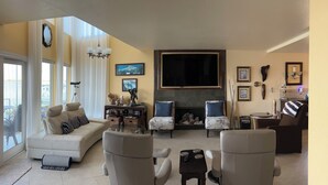 Una sala de estar con un sofá, dos sillones, una chimenea, un televisor y un comedor con mesa y sillas.