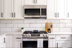 Una cocina moderna con armarios blancos, una estufa de acero inoxidable, un microondas y un juego de cuchillos.